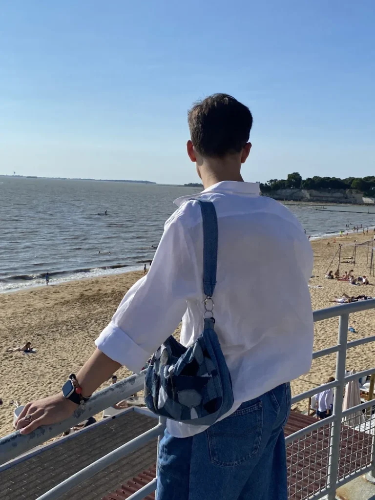Patch Bag en denim recyclé porté à la plage avec une chemise blanche